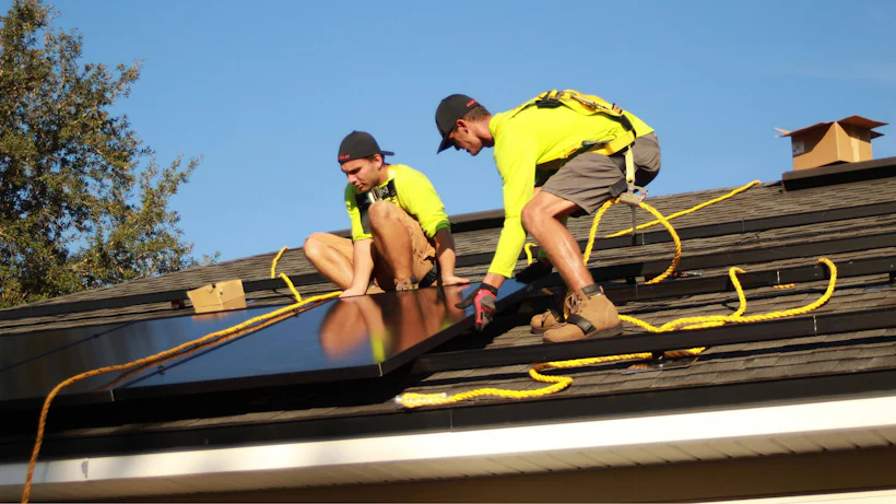 Dois instaladores com equipamento de segurança fixando módulos fotovoltaicos no telhado